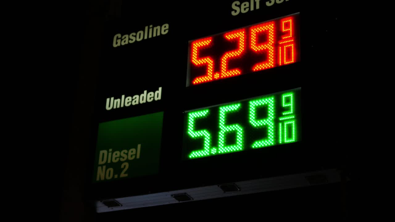Gas station prices LED light up sign for regular and diesel fuel at night over 5 dollars per gallon credit and cash price, during 2021 2022 war time recession, ground up shot twisting zooming in