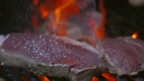 Chef-Dropping-Salt-Seasoning-onto-Raw-Sirloin-Steaks-as-it-Cooks-on-Flame-Grilled-BBQ-in-Slow-Motion-4K