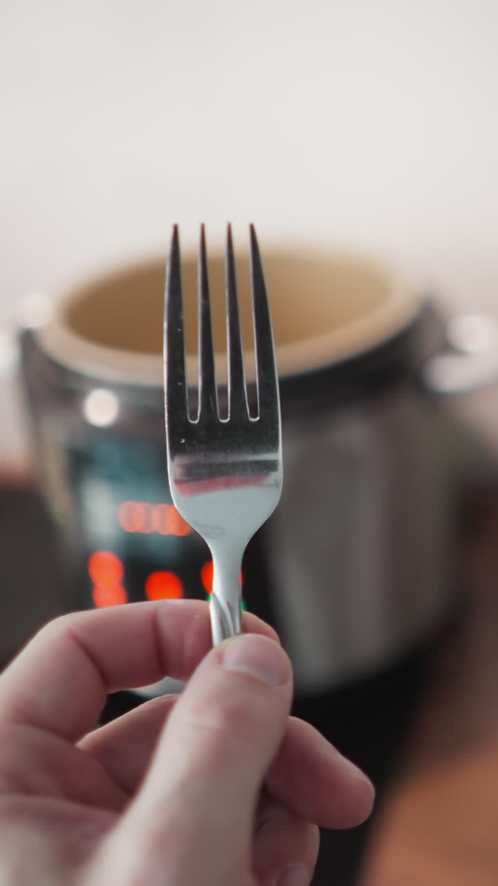 pov de mano de una persona que sostiene un tenedor acercándose a una mesa de cocina con una cocina múltiple parpadeando luces en el fondo