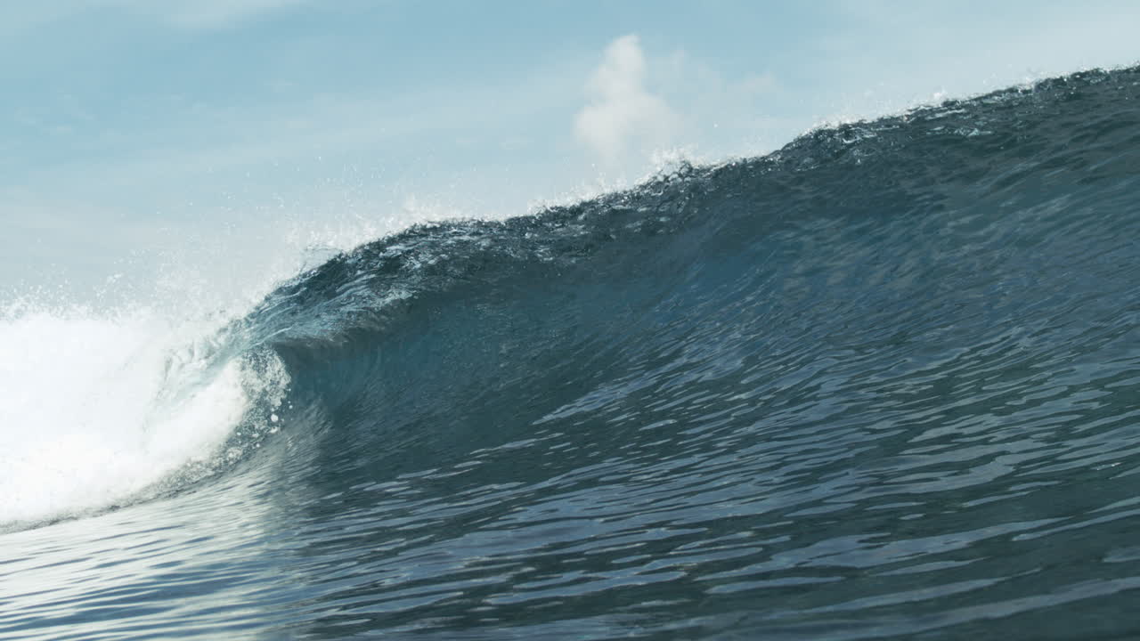 Large wave rolling steadily through calm ocean under cloudy afternoon light