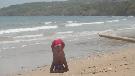 Contorsión-Chica-Flexible-En-Bikini-Haciendo-Un-Soporte-De-Mano-Con-Olas-Del-Océano-Rompiendo-En-El-Fondo