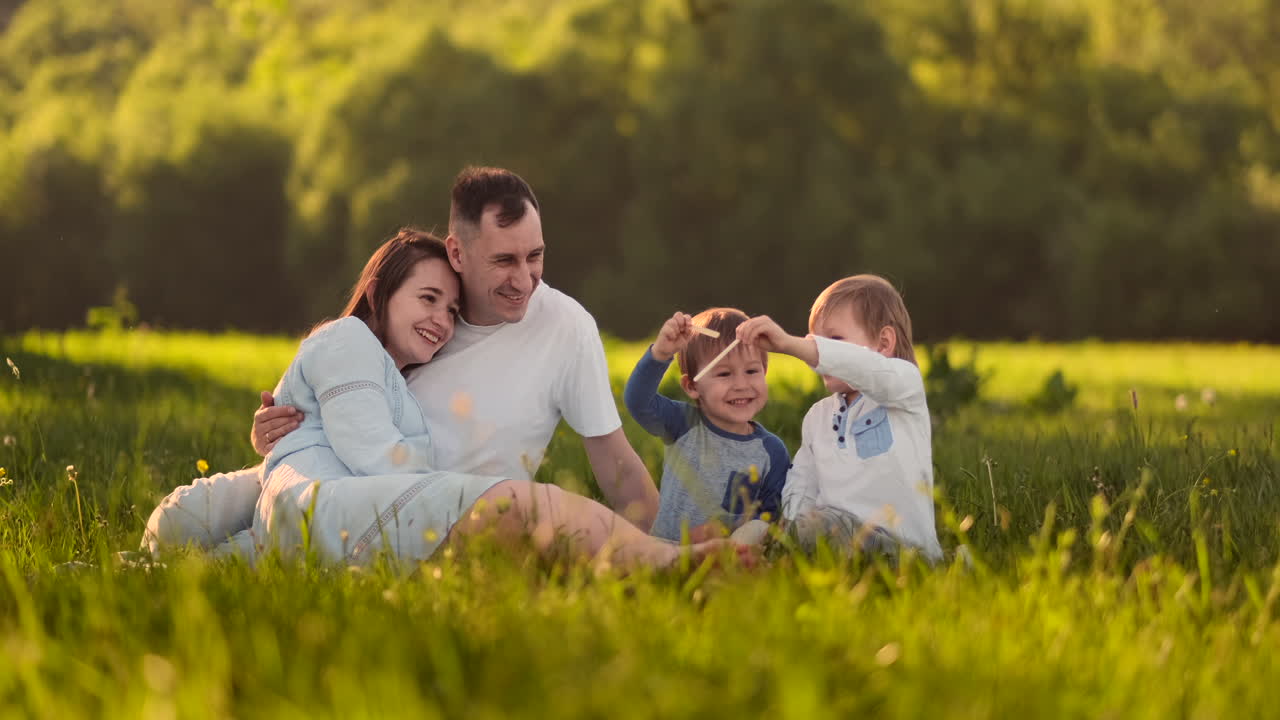 мама с двумя сыновьями летом на закате, сидя на луге на траве, смеясь и обнимаясь.
