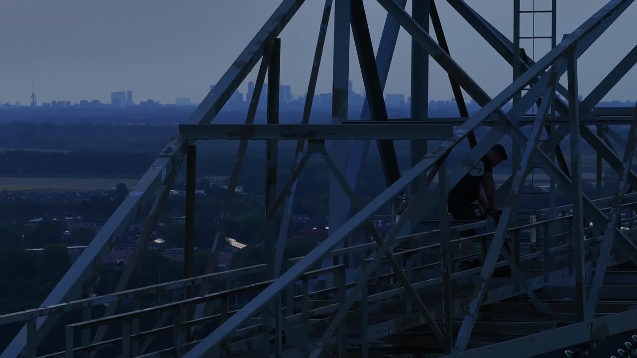 Person standing on an industrial structure at dusk with a view of the city in the background