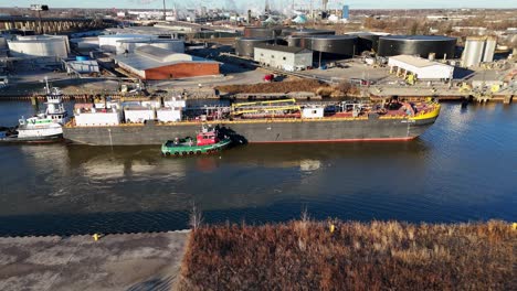tugboats moving massive barge in maumee river, industrial area behind, aerial view