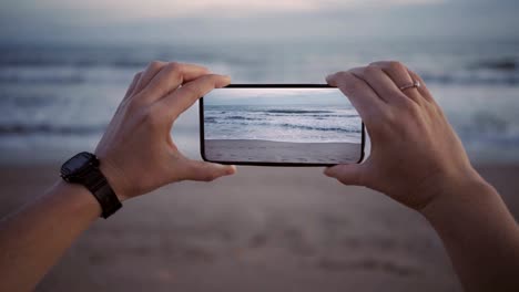 filmando olas en la playa al crepúsculo en un nuevo teléfono inteligente con pantalla ancha