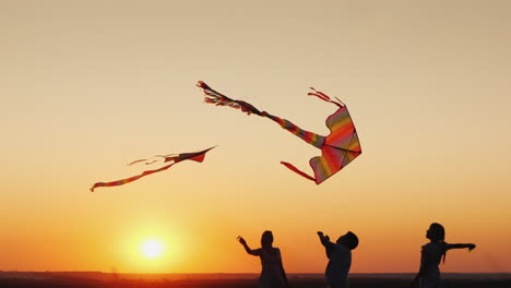 two children with mom play kites at sunset good time together