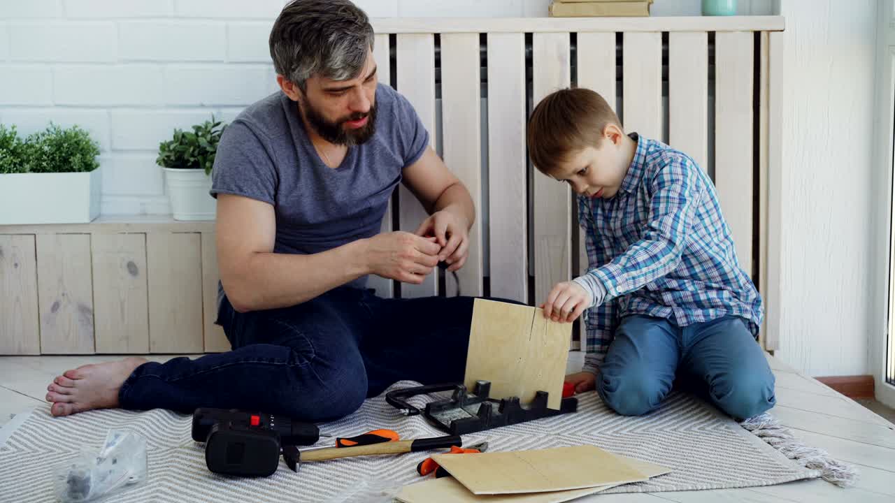 padre barbudo y pequeño hijo lindo haciendo una casa de pájaros de sábanas de madera en casa. concepto de la infancia y la paternidad haciendo high-five para celebrar el trabajo exitoso.