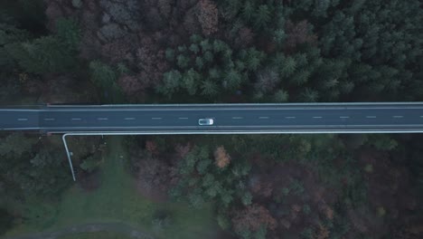 top down aerial view of white electric car moving on elevated road in twilight, high angle drone shot