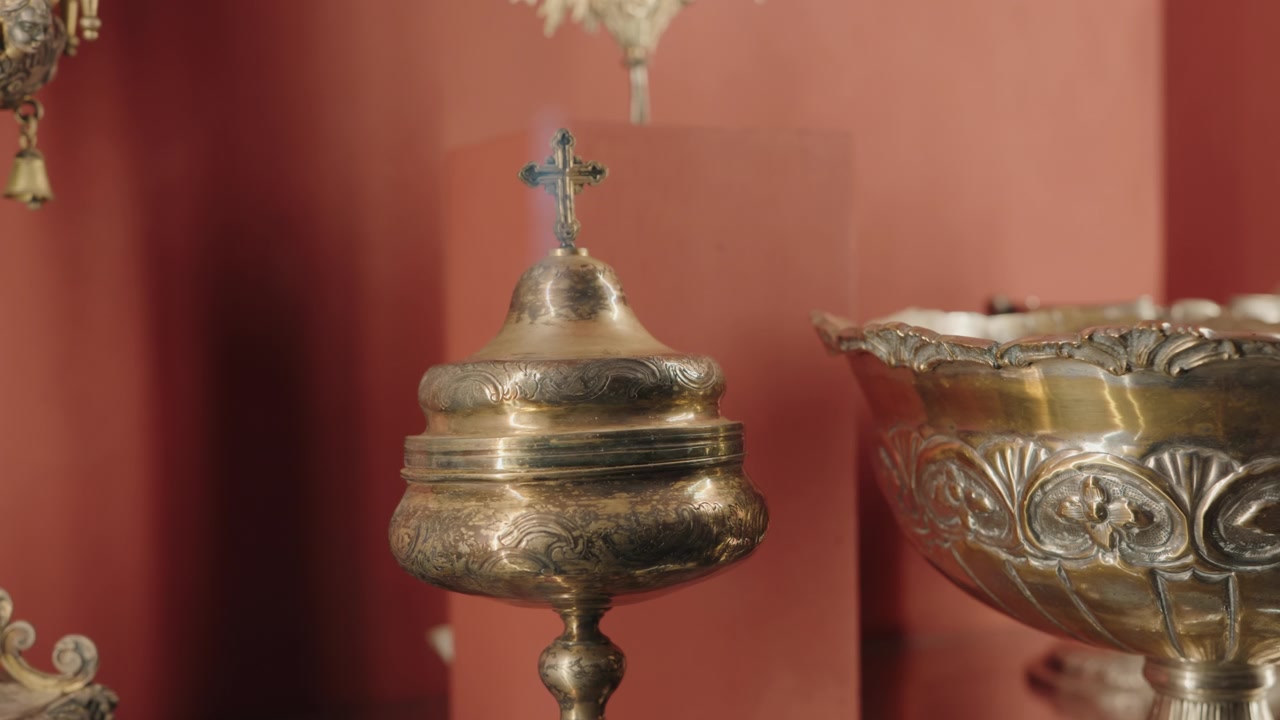 Engraved silver ciborium topped with cross beside gilded chalice on red background
