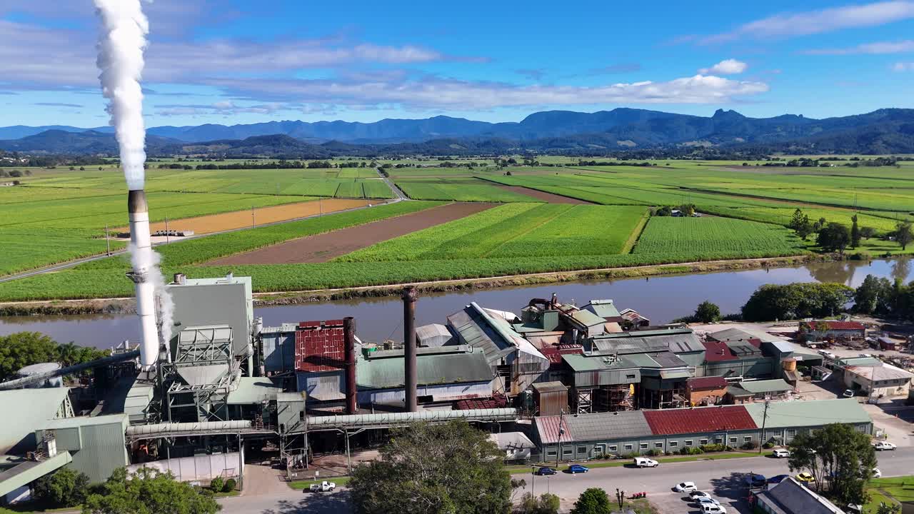 Aerial footage of a sugarcane factory with surrounding fields, showcasing industrial activity and rural landscape under clear skies