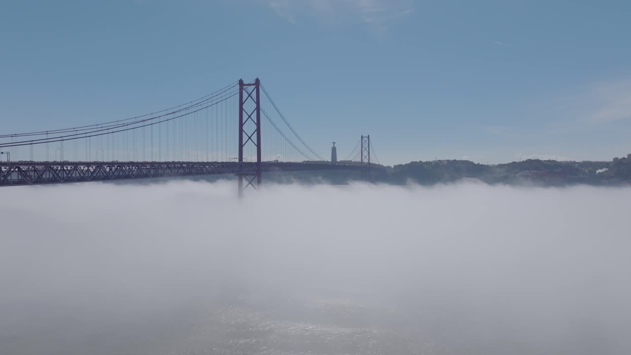 Drone shot ascending through the fog revealing the bridge in Lisbon.