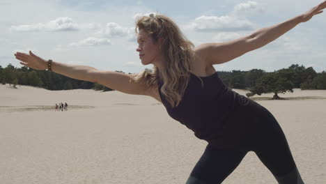 beautiful woman doing half moon pose in sand dunes