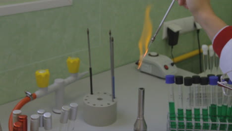 en un laboratorio de ciencias, se crea una llama naranja colorida cuando se produce una reacción química alrededor de una pipeta delgada que el científico sostiene sobre una llama abierta