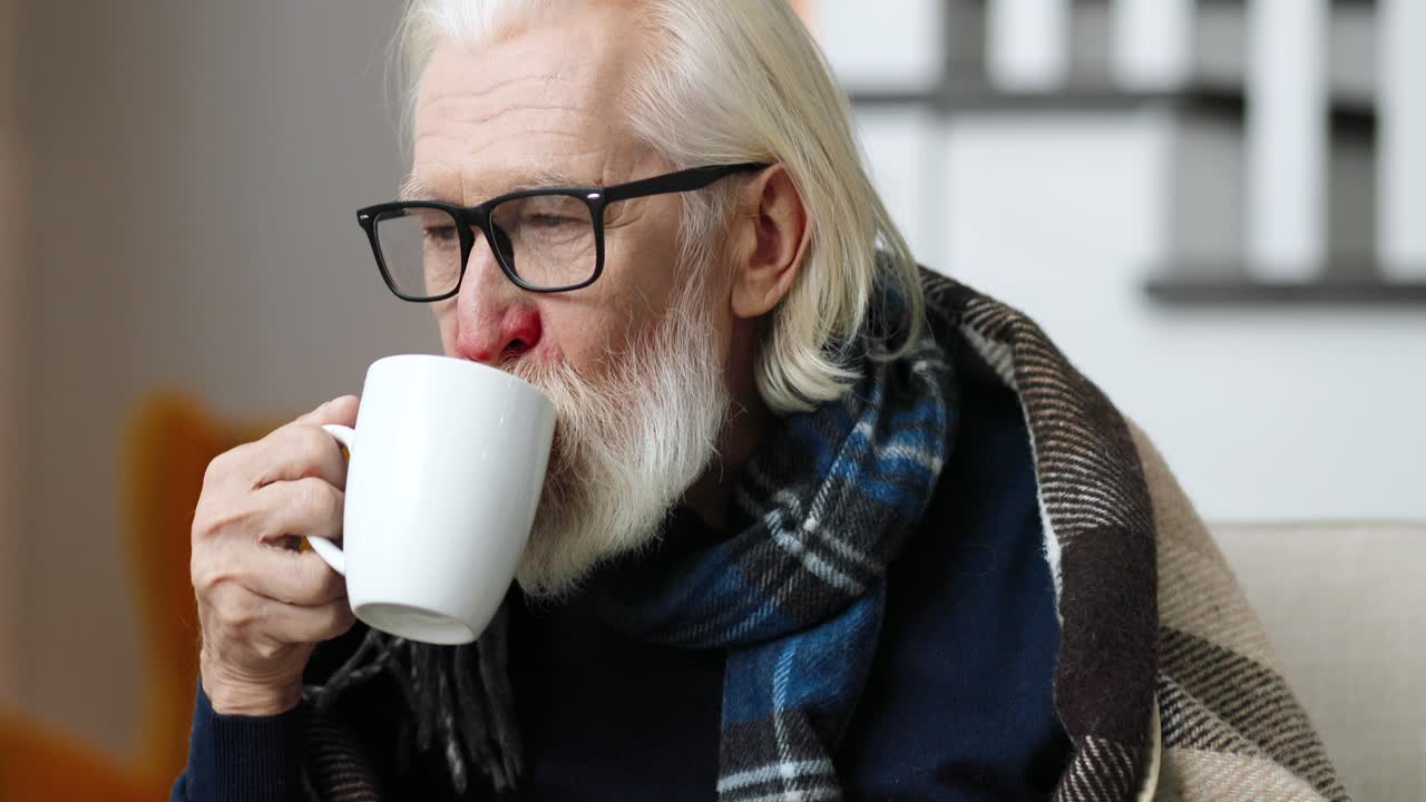 hombre enfermo sentado en casa y bebiendo una bebida caliente mientras mira hacia otro lado