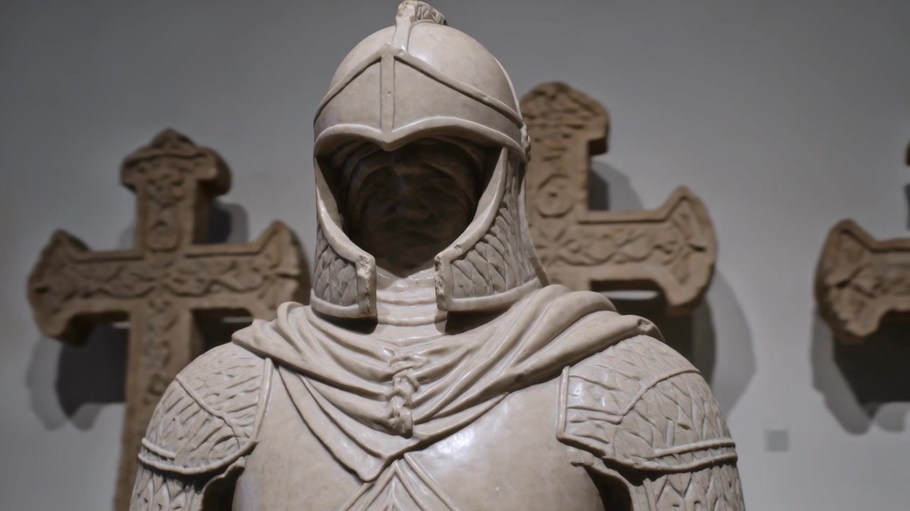 Telecamera panoramica che rivela un cavaliere di pietra intagliato con mantello e spallacci in un museo, croci di pietra.