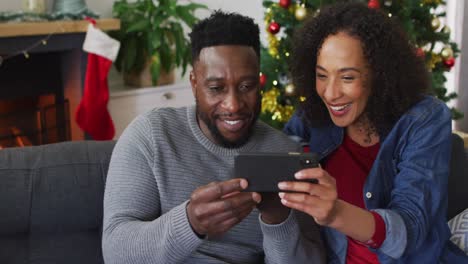 Smiling-african-american-couple-having-video-call-and-gesturing,-christmas-decorations-in-background