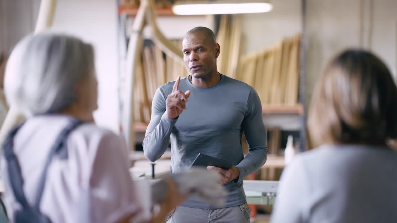 Man Speaking and Gesturing to Two Women in a Workshop
