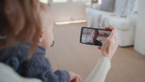 Mutter-Und-Baby-Unterhalten-Sich-Per-Smartphone-Per-Video-Chat-Mit-Dem-Vater,-Der-Dem-Säugling-Auf-Dem-Bildschirm-Zuwinkt-Und-Genießen-Die-Kommunikation-Mit-Der-Familie-über-Eine-Mobiltelefonverbindung-In-4K