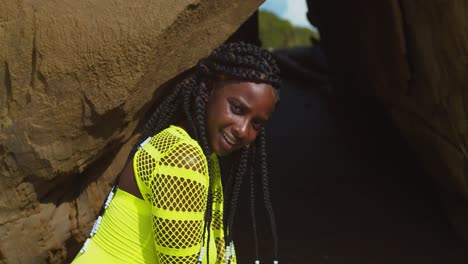 menina negra de cabelo natural ajoelhada na entrada de uma caverna de biquíni