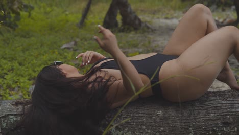 hispanic girl playing in her hair while laying on a fallen tree trunk in a forested area at the beach