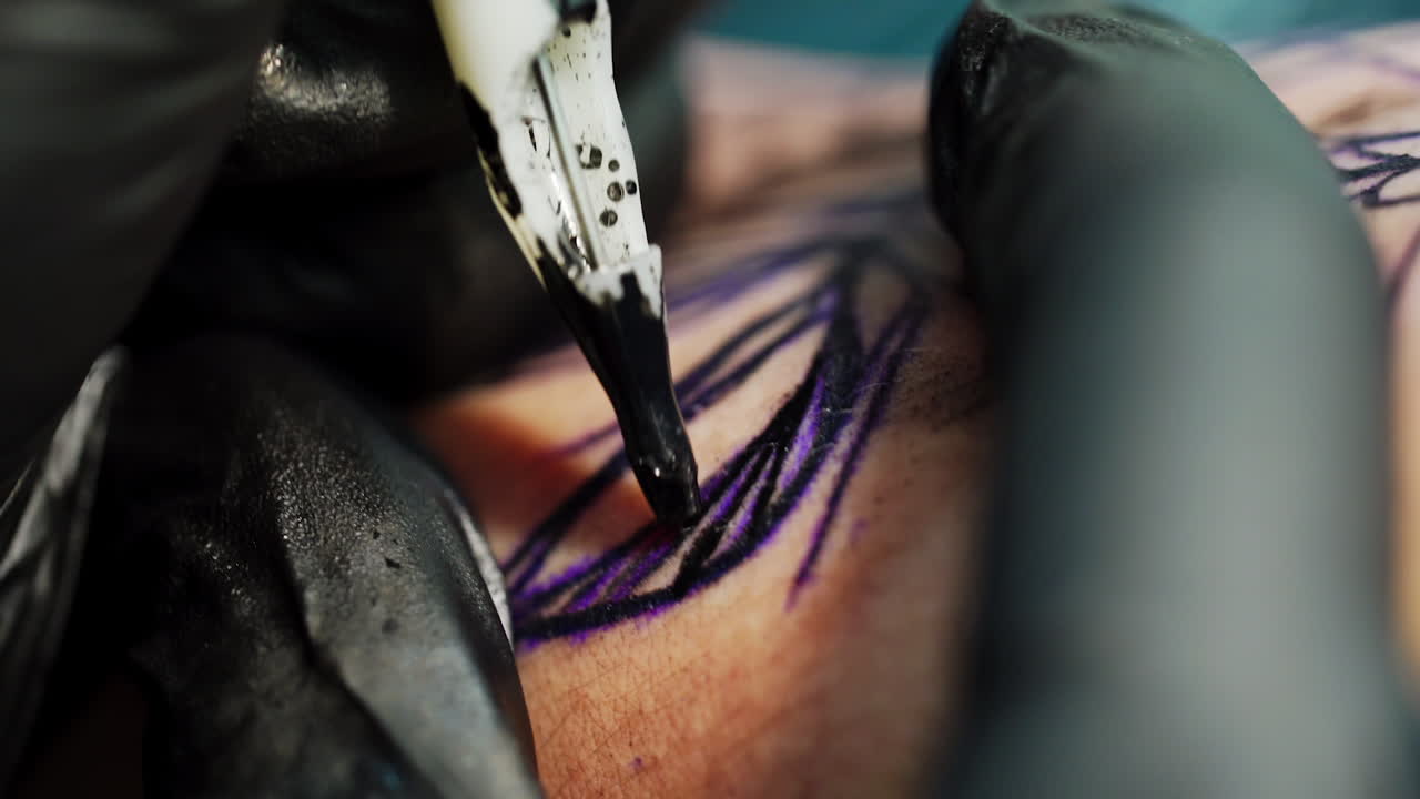 Tattoo machine putting the ink on the sketch. Black gloved hands hold and stretch the skin. Close up.