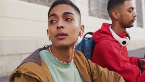 Two-mixed-race-male-friends-wearing-headphones,-listening-to-music-in-the-street