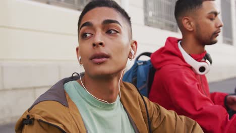 dos amigos varones de raza mixta con auriculares, escuchando música en la calle