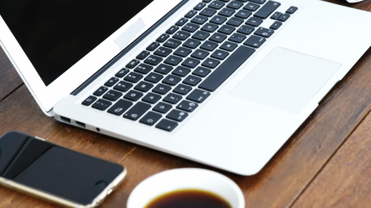 portátil, teléfono móvil, cuaderno y taza de café dispuestos en una mesa de madera