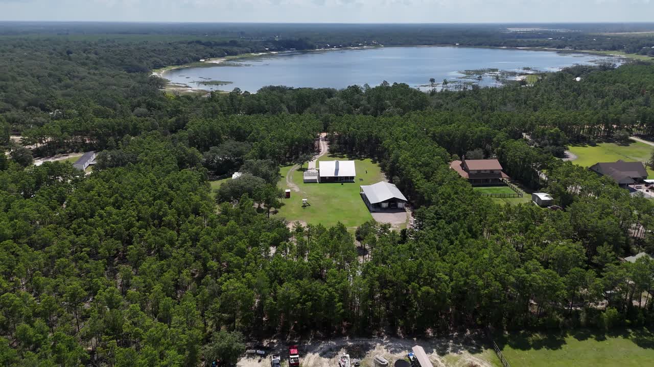 Dynamic backward drone movement from a private rural farmland with barn and surrounding green forest trees, Panama City Beach, Florida, USA