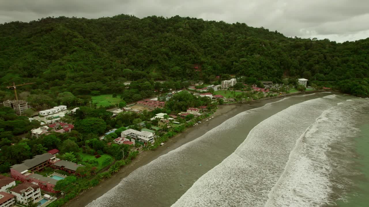 aérea sobre la playa costera con olas marinas salpicando las orillas, casas y pequeños asentamientos residenciales visibles