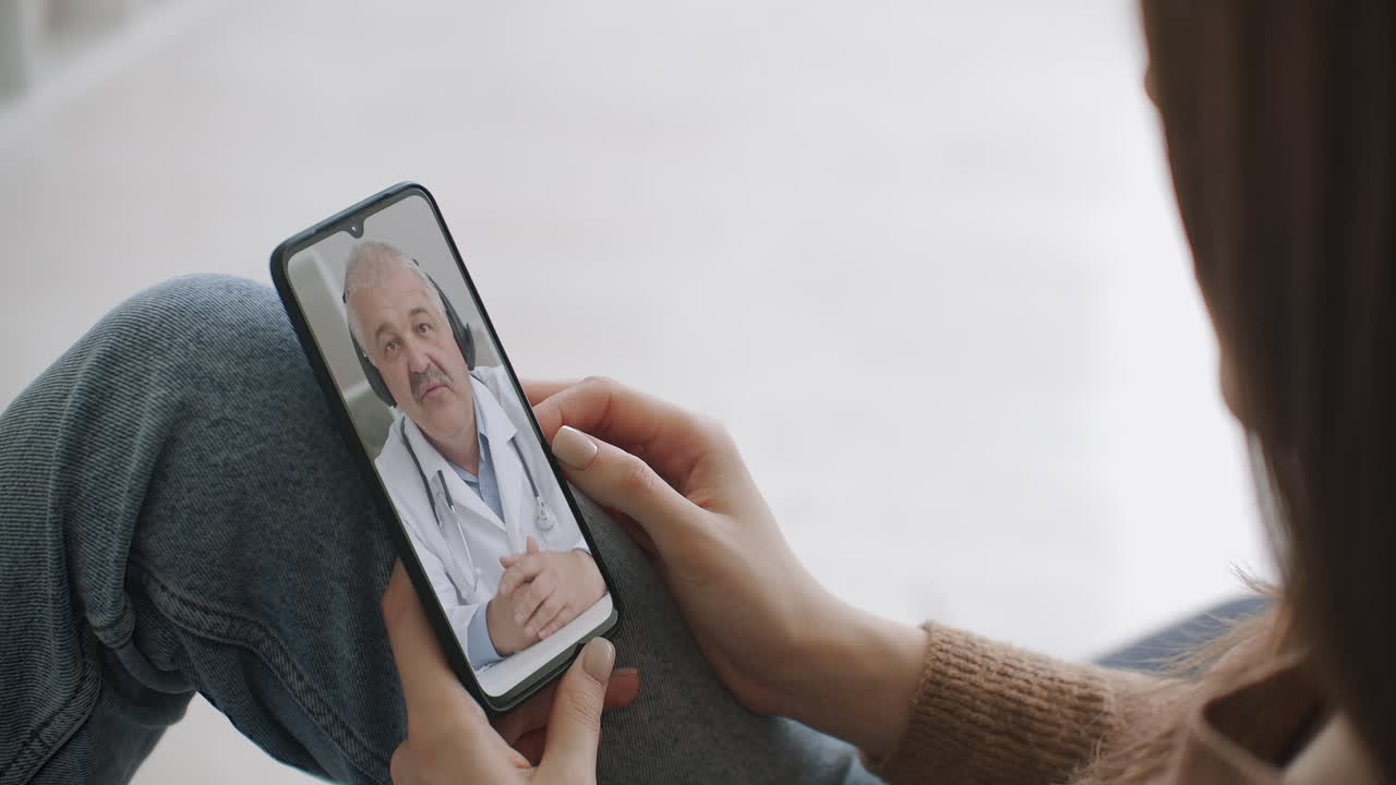 Woman using medical app on smartphone consulting with doctor via video conference. Female using online chat to talk with family therapist and checks possible symptoms during pandemic of coronavirus.