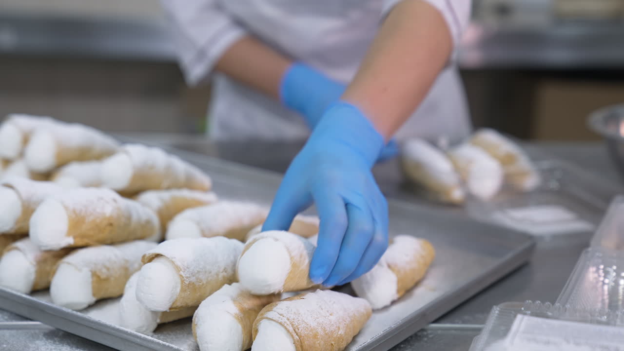 Cannoli desserts with white whipped cream and sugar powder on top. Woman worker puts sweets into plastic package. Close up.