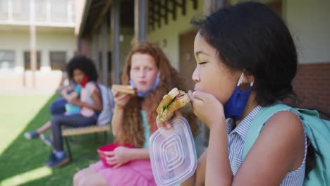 dos niñas comiendo el almuerzo de la caja de tiffin mientras están sentadas en un banco en el parque en la escuela