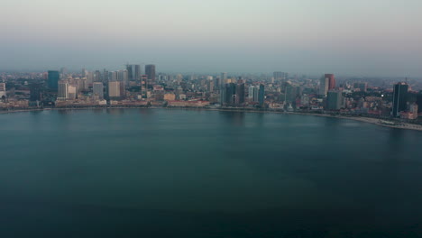 Traveling-right,-Luanda-city,-golden-hour-flying-over-Luanda-bay,-Africa
