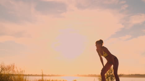 athletic girl playing beach volleyball jumps in the air and strikes the ball over the net on a beautiful summer evening. caucasian woman score a point.