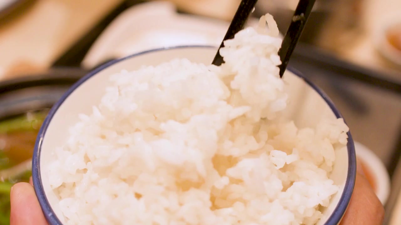 Persona che usa le bacchette per mangiare riso bianco al vapore da una ciotola