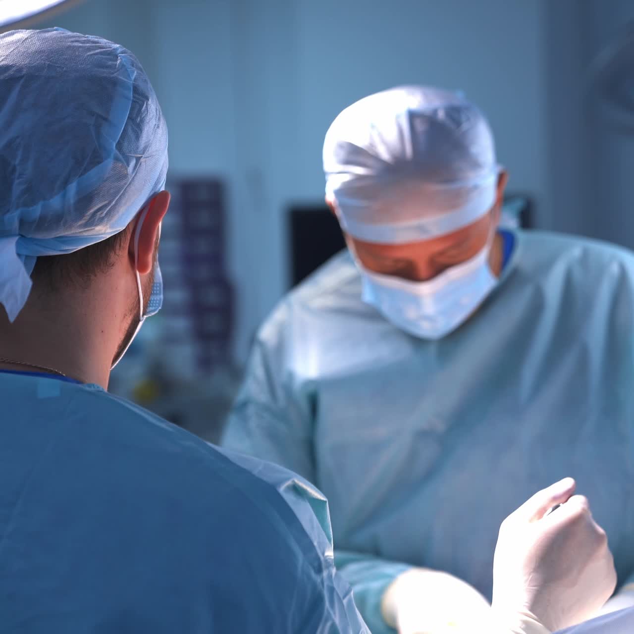 Assistente in sala operatoria che tiene in mano uno strumento sopra il paziente. Primo piano. Il chirurgo primario lavora all'operazione in modo sfocato sullo sfondo.