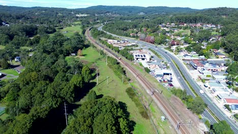 Landschaft-Mit-Zügen-Auf-Gleisen-Und-Autos-Auf-Der-Hauptstraße-In-Der-Nähe-Des-Buschlandes-Der-Vororte-Von-Ourimbah-An-Der-Central-Coast,-Reisen,-Tourismus,-Transport,-Drohnenluftaufnahmen,-Australien