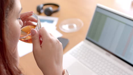 Mujer-Birracial-Enfocada-De-Talla-Grande-Bebiendo-Té-Mientras-Usa-Una-Computadora-Portátil,-Trabajando-Desde-Casa,-Cámara-Lenta