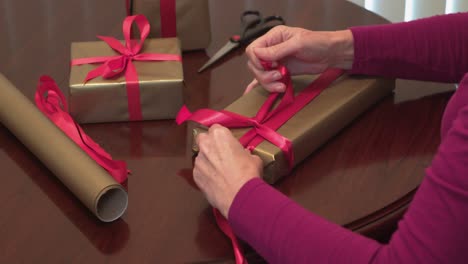 closeup hands tying red ribbon on christmas gifts