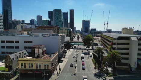 Vista-Aérea-De-Wellington-Street-En-La-Estación-De-Metro-De-Perth-Con-Una-Pasarela-Peatonal-Y-Cruzando-La-Calle-Y-El-Rascacielos-Al-Fondo,-Perth,-Australia-Occidental