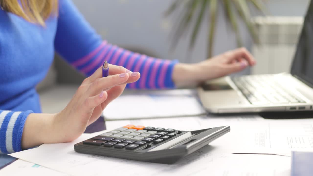 mujer usando calculadora para calcular facturas domésticas en el hogar, haciendo papeleo para pagar impuestos