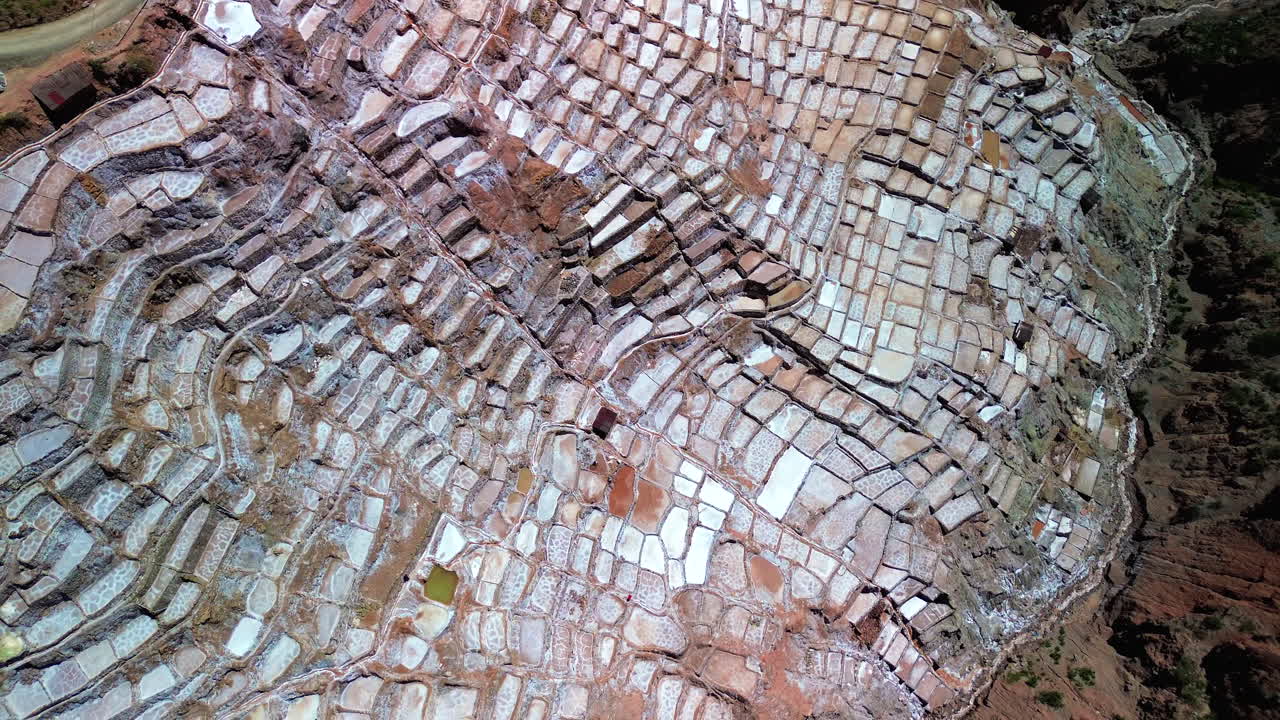ángulo aéreo alto de arriba hacia abajo pan a través de las históricas minas de sal de mara en perú, vibrantes terrazas antiguas en un entorno exuberante