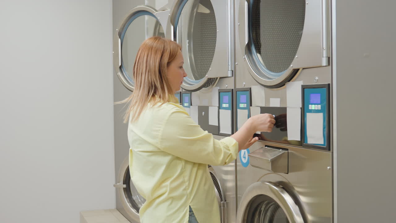 Joyful woman closes industrial washing machine filter drawer after inserting cleaned inner filter, pushing it back into compartment and locking with key while working inside laundromat environment