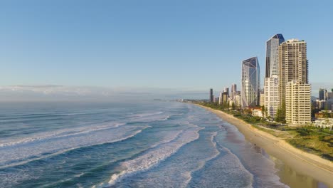 aerial footage captures the gold coast's stunning beachfront skyline under clear skies, showcasing waves and high-rise buildings
