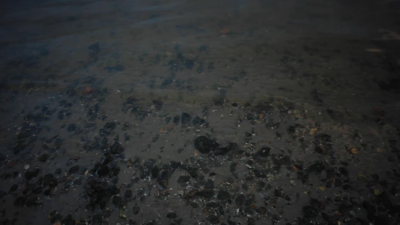 Shallow bay waters sway peacefully; water is transparent and sand with rocks clearly visible at the bottom. Sun has set. Footage in HD