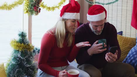 Feliz-Pareja-Madura-Caucásica-Haciendo-Videollamadas-En-Una-Habitación-Llena-De-Adornos-Navideños