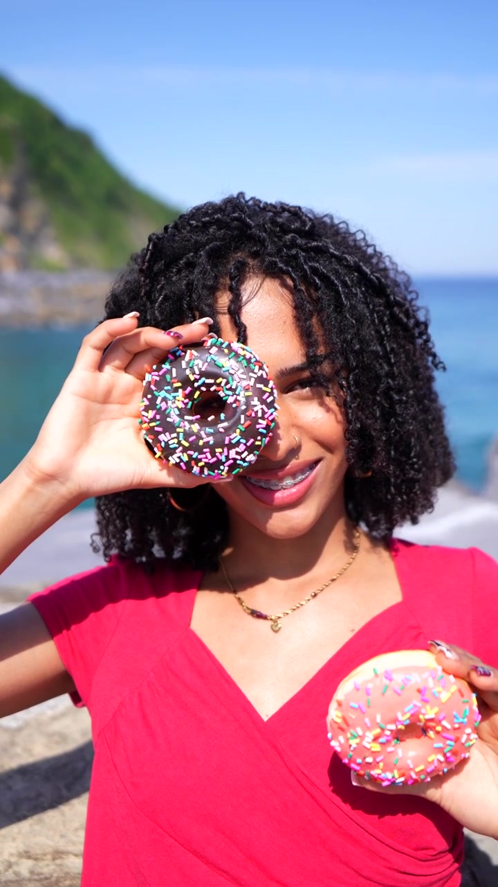 Giovane donna felice in posa con ciambelle colorate in riva all'oceano