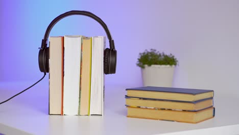 auriculares negros con una pila de libros sobre fondo azul. libros de audio o concepto de educación.