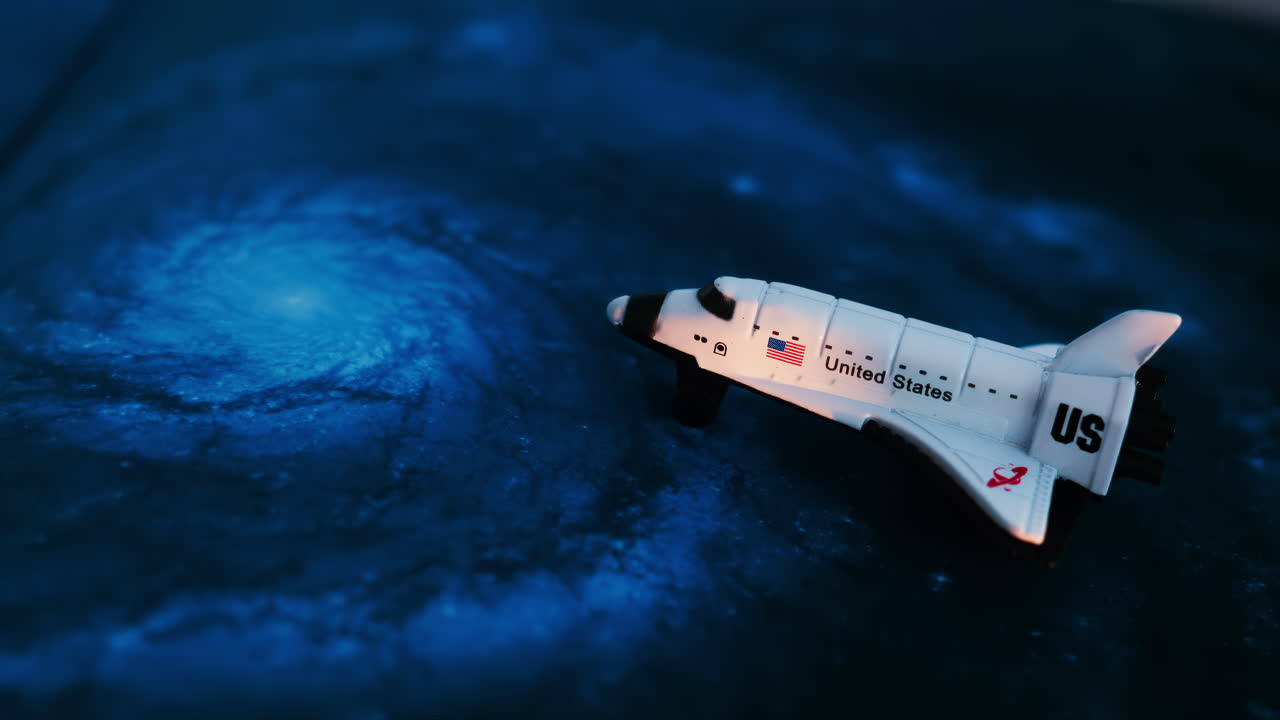 Close up of a miniature toy space shuttle placed on a blue cosmic galaxy backdrop